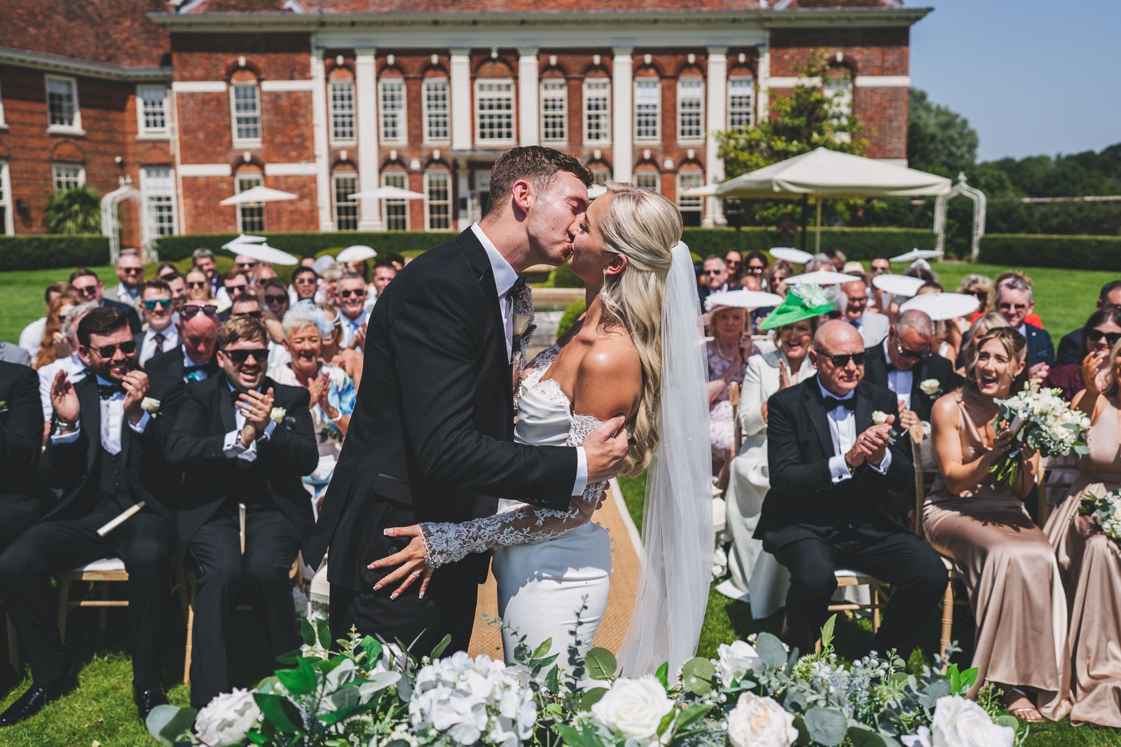 Couple kissing at the end of an outdoor ceremony as guests applaud